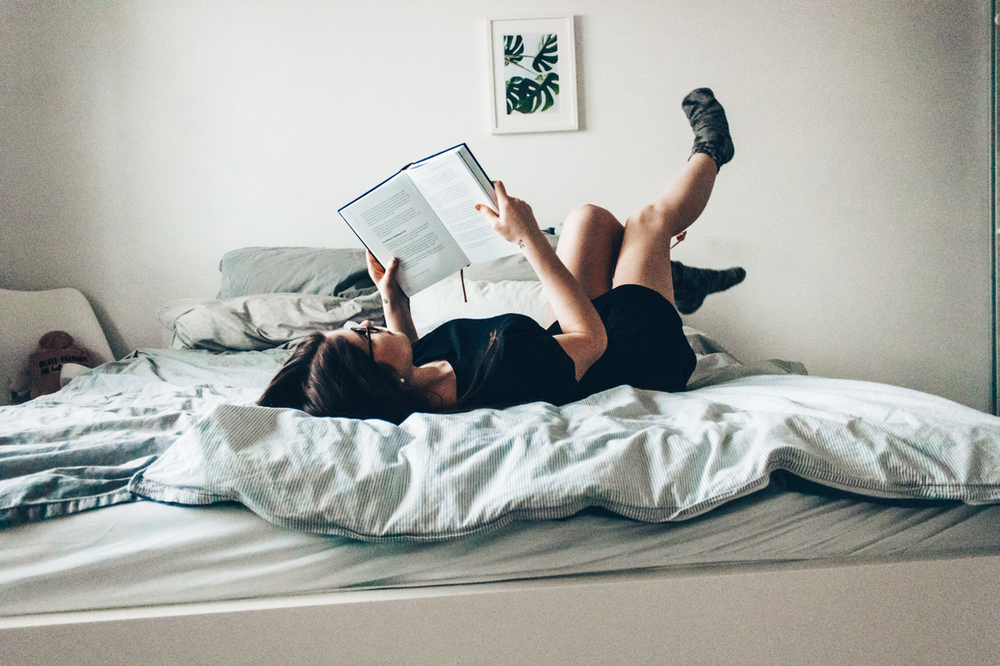 woman reading a book on her bed with legs up in the air