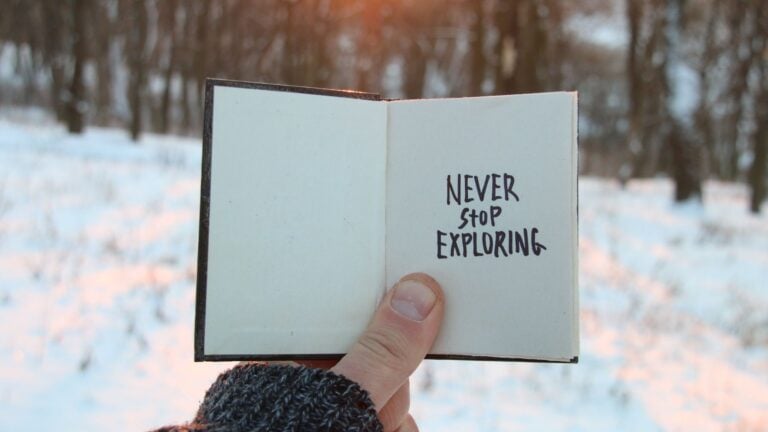 a tiny book with the quote "never stop exploring? written on it and someone holding it up outside in a winter setting