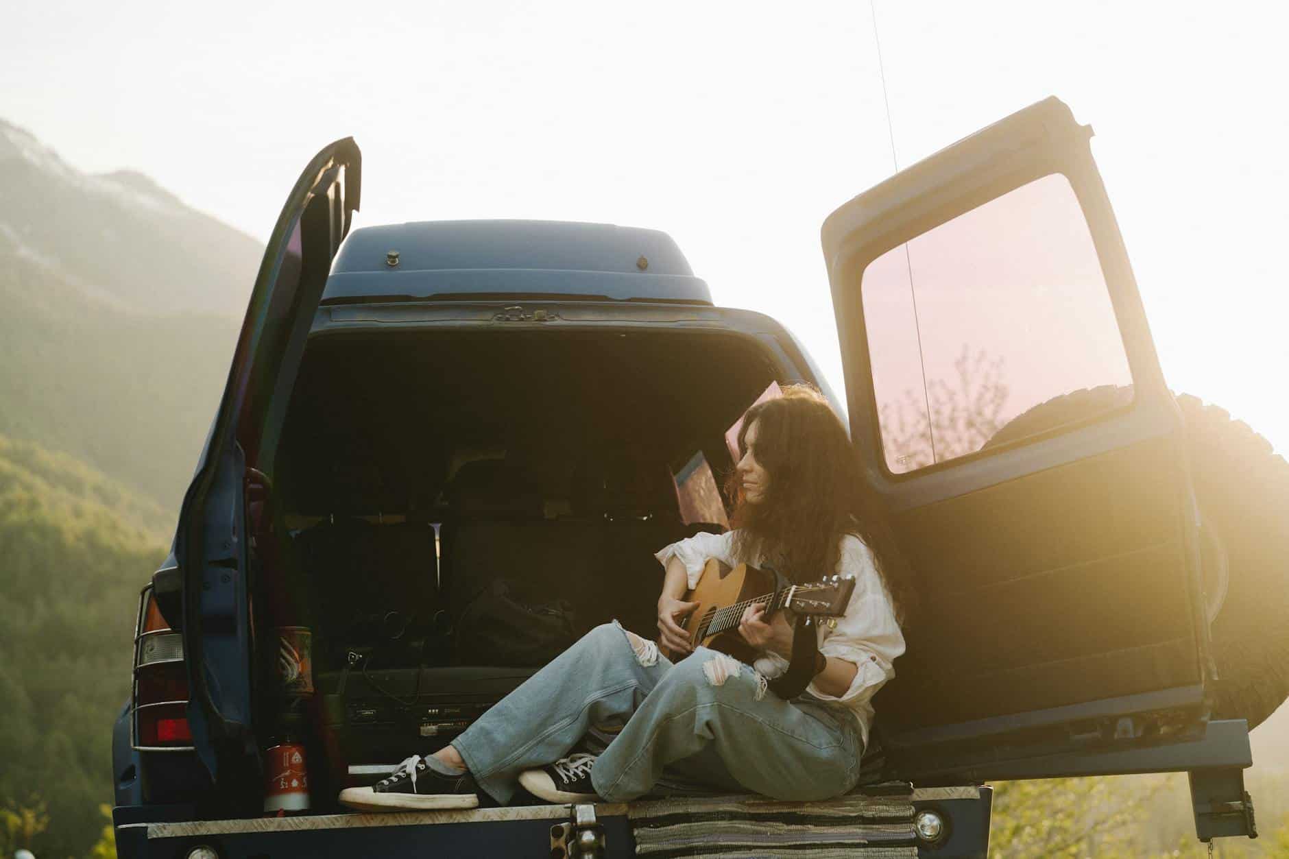 a woman playing the guitar at the back of a van