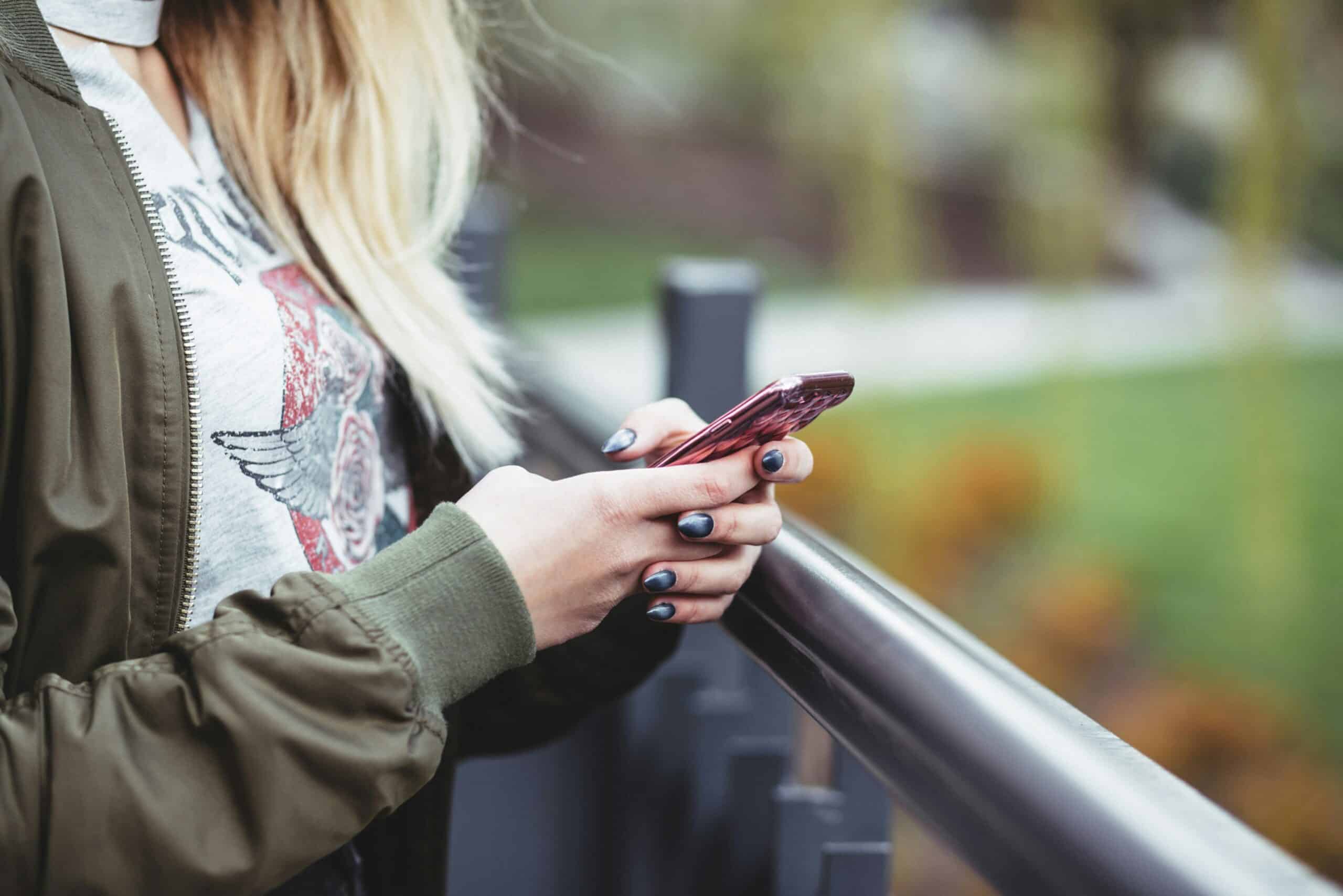 Woman using smartphone outdoors for somatic prompts and self-discovery.