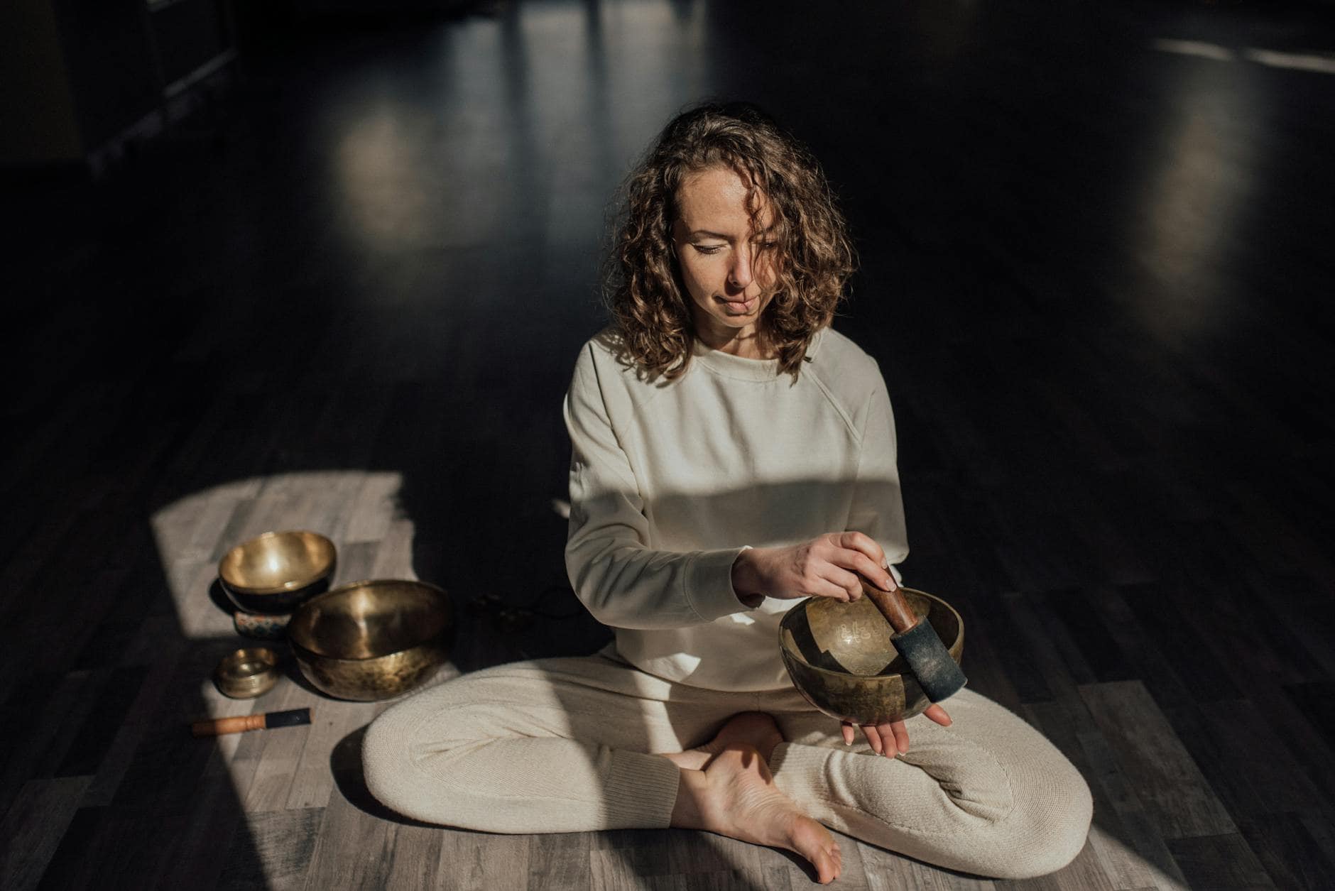 spiritual practitioner playing bowl gong on floor in sunlight