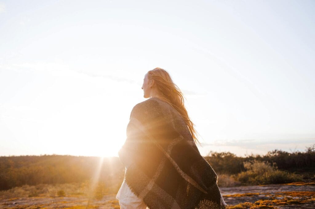 a woman wrapped in plaid blanket backlit by the sunset