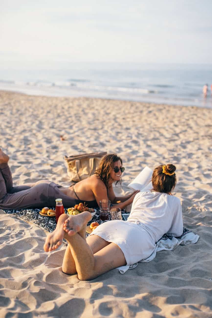 women lying on the beach while having conversation