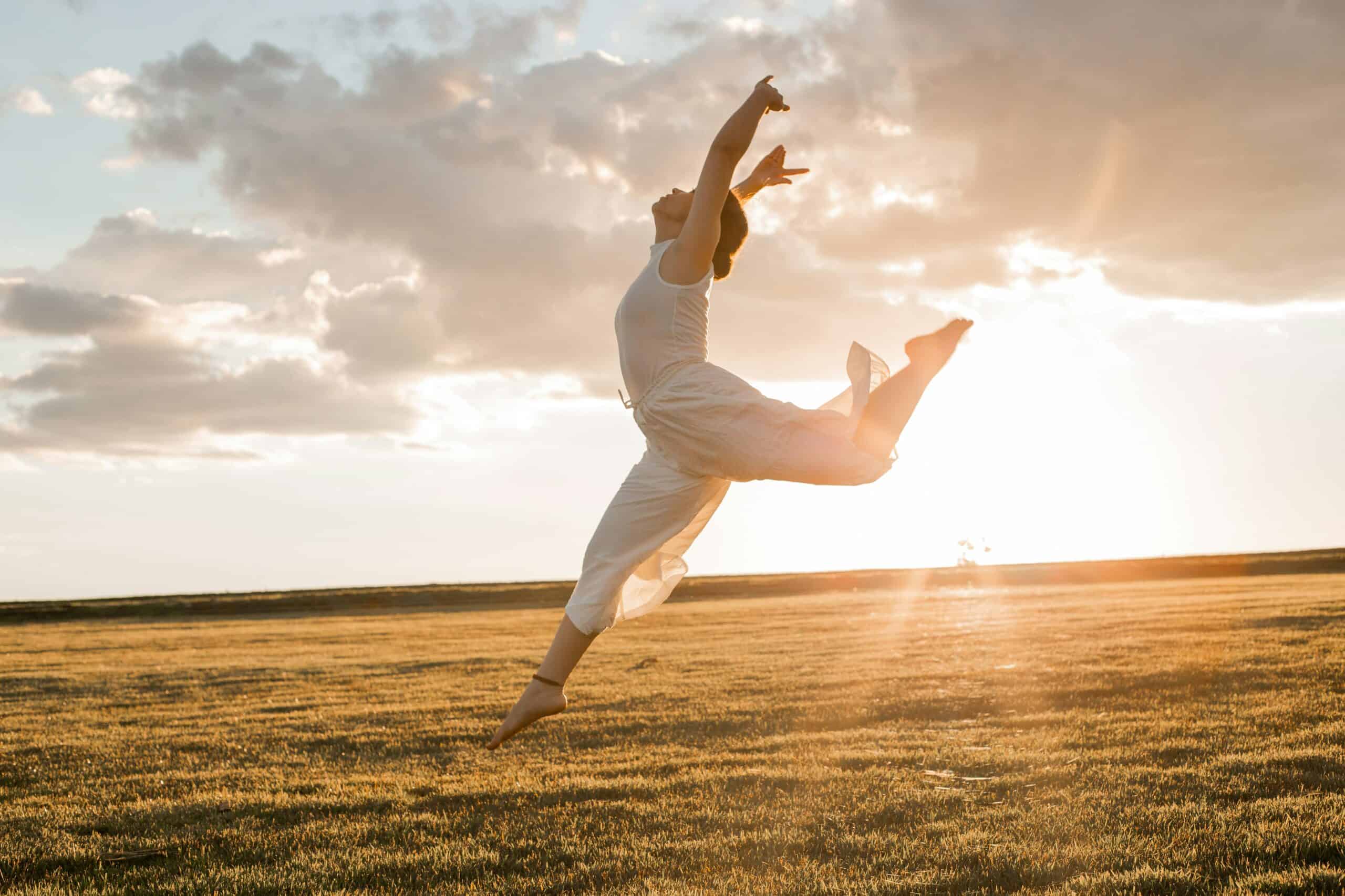 Woman jumping in open field during sunset, symbolizing energy flow and self-awareness.