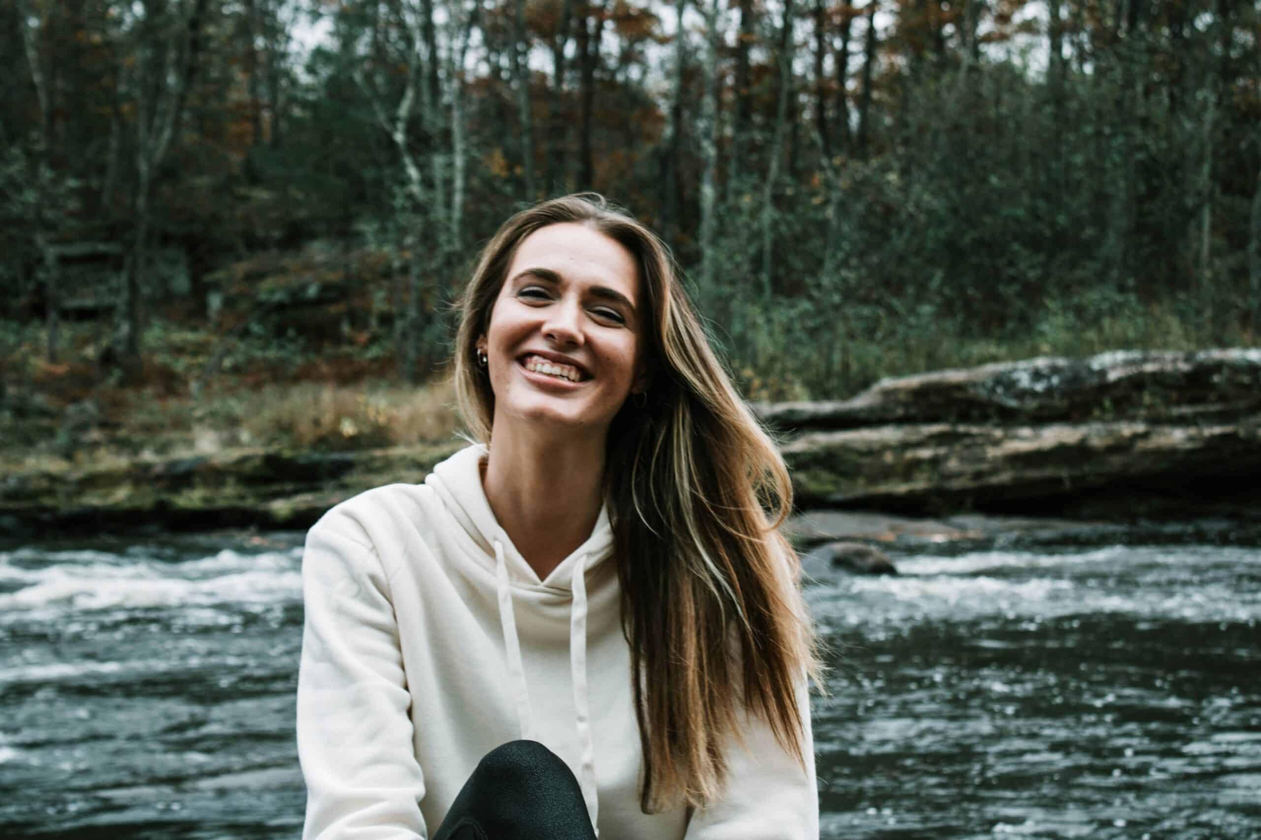 Happy woman outdoors by river promoting healthy mindset and mental well-being.