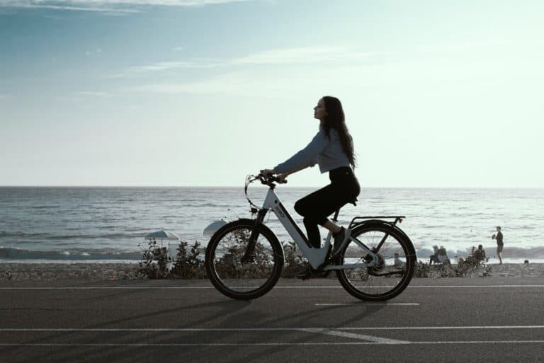 Woman riding a bicycle along the beach during daytime, symbolizing energy flow and cycle awareness.