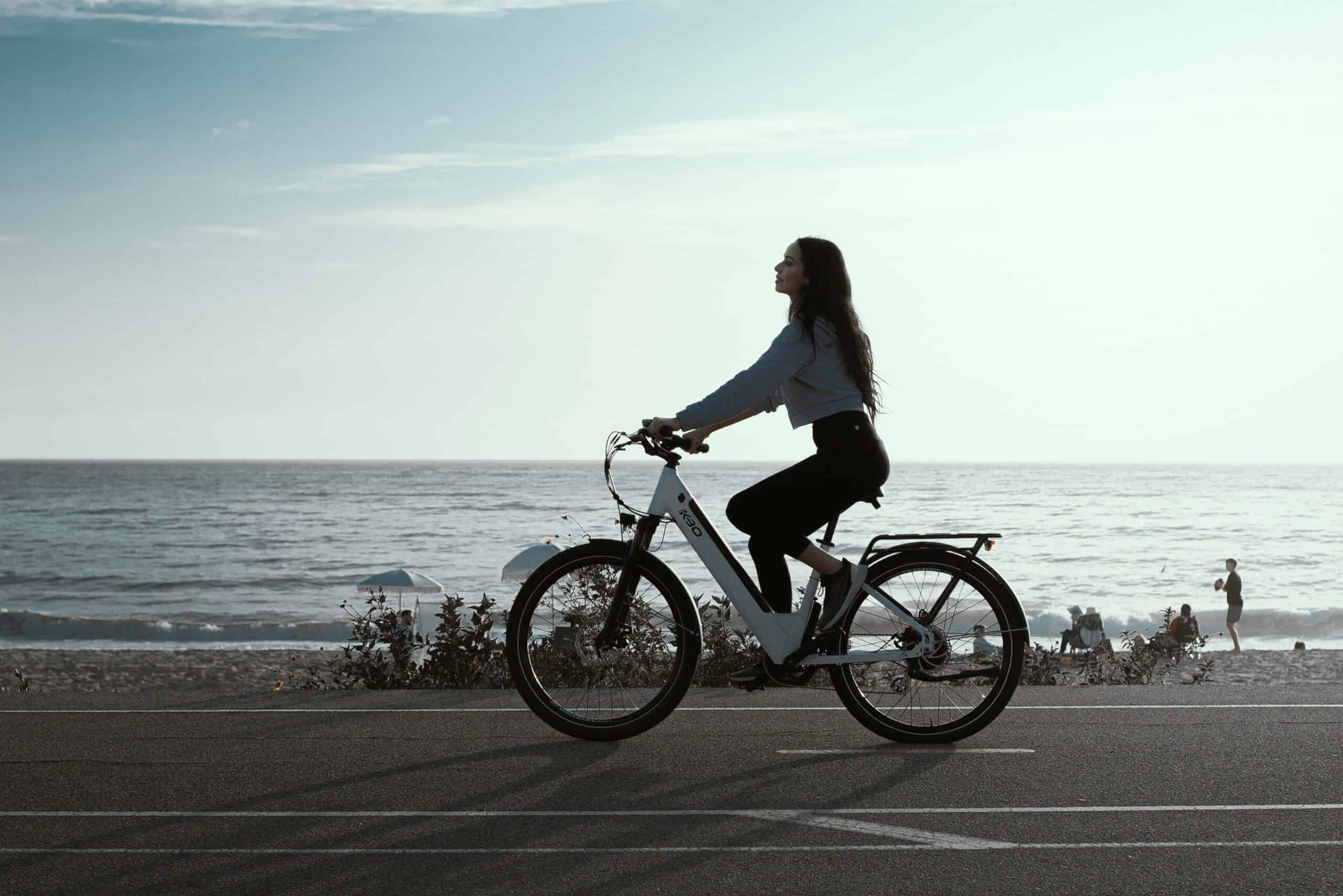 Woman riding a bicycle along the beach during daytime, symbolizing energy flow and cycle awareness.
