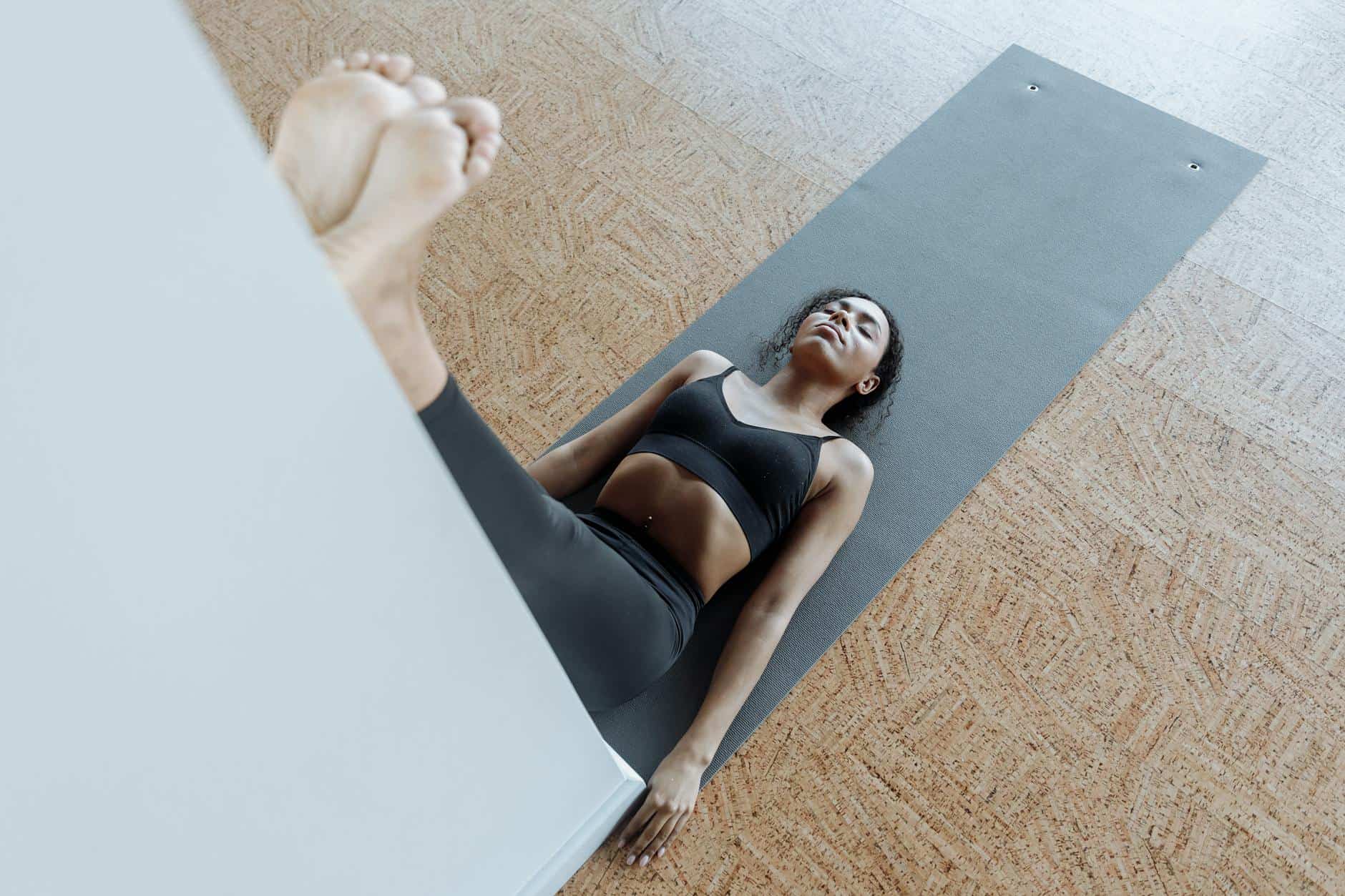 woman in black active wear lying on a yoga mat while leaning her legs on the wall