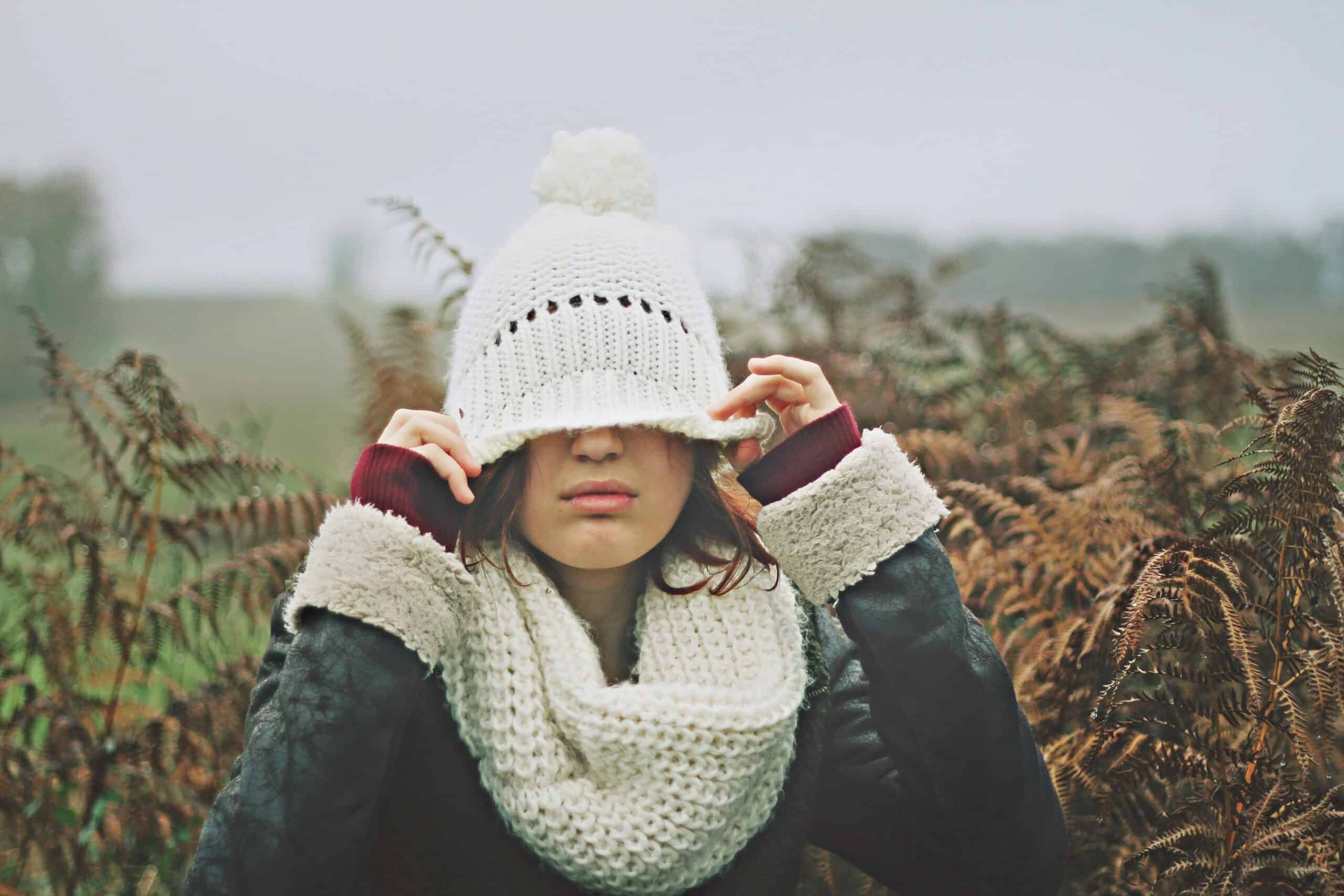Woman in winter clothing covering her eyes, symbolizing emotional exhaustion and burnout.