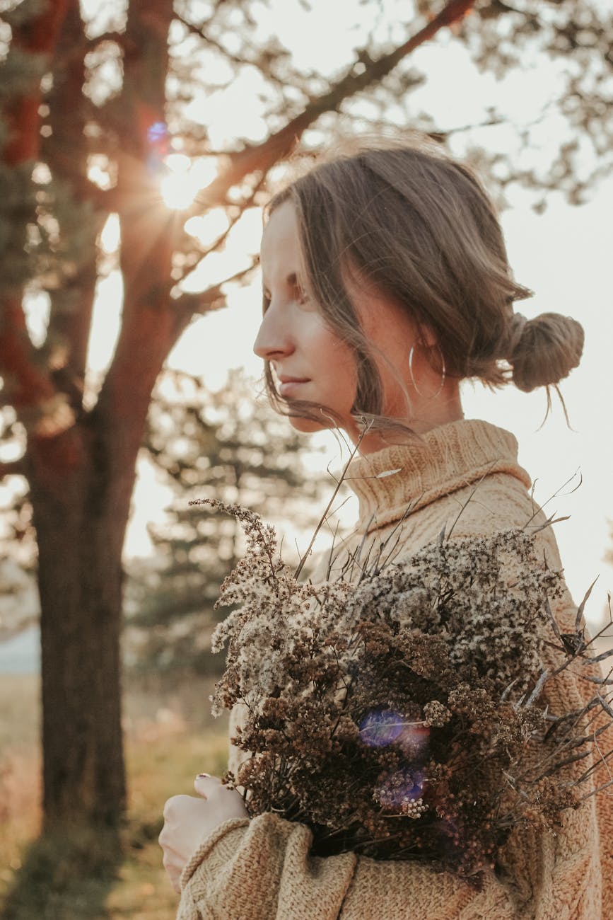 woman in beige knitted sweater holding a bunch of dried flowers