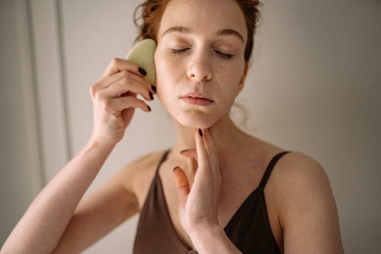 Young woman using jade stone for facial gua sha massage, focusing on self-care and skincare routine.