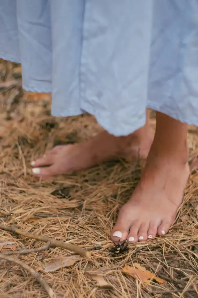 Bare feet in white dress on pine straw