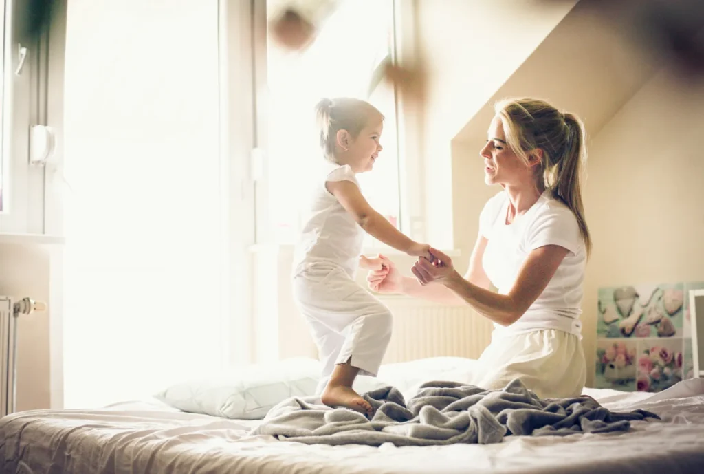 Mom and toddler playing on sunlit bed