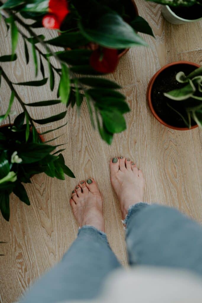 Person standing barefoot on wooden floor with houseplants, promoting desk-based body resets.