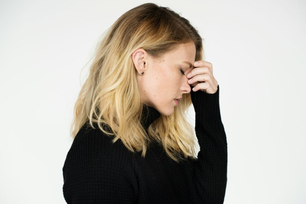 Relaxed woman with hand on forehead, experiencing stress or nervousness, in a minimalistic setting.