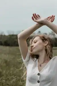 Woman Arms Crossed Overhead Eyes Closed In Field Woman arms crossed overhead eyes closed in field