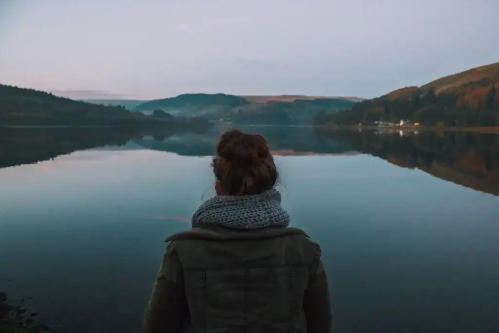 Woman by still lake at dusk with scarf