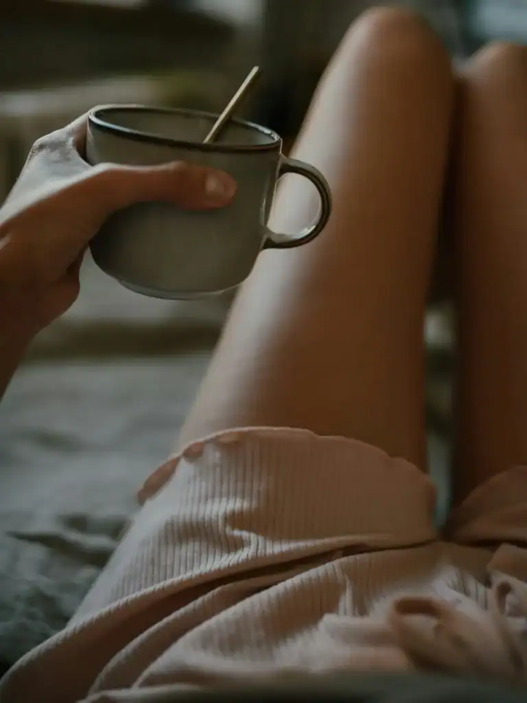 Woman holding mug legs up on bed