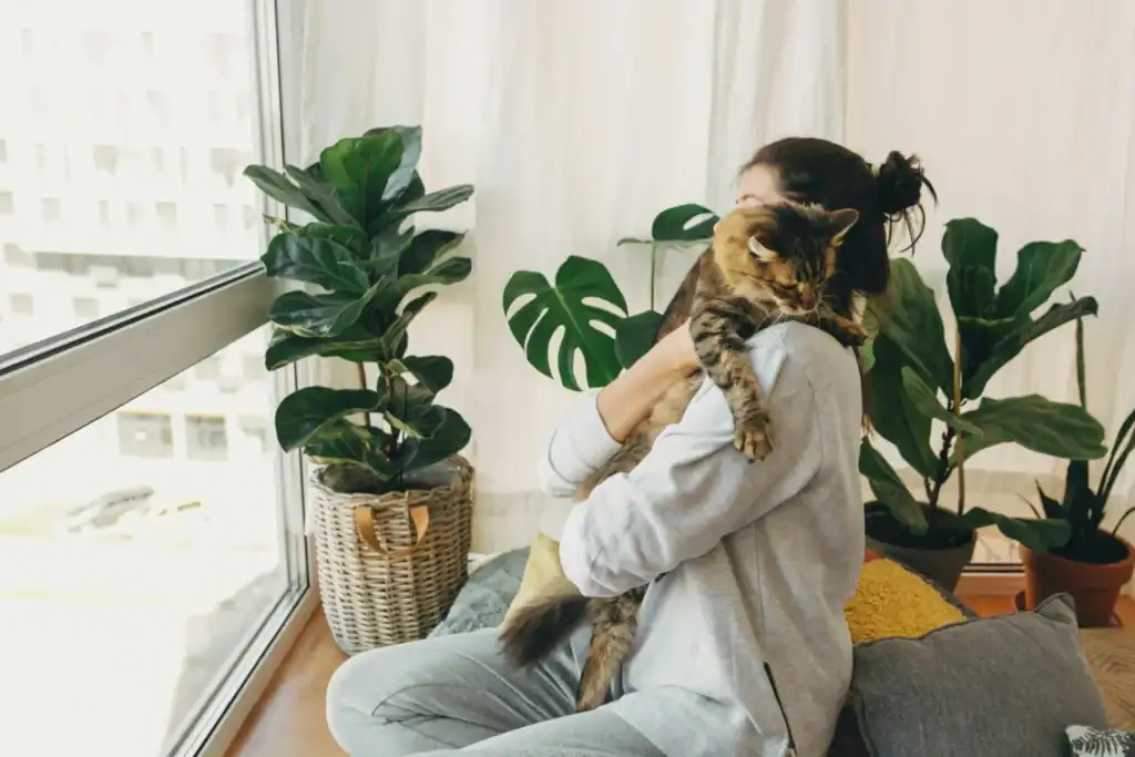 Woman holding tabby cat in plant filled apartment