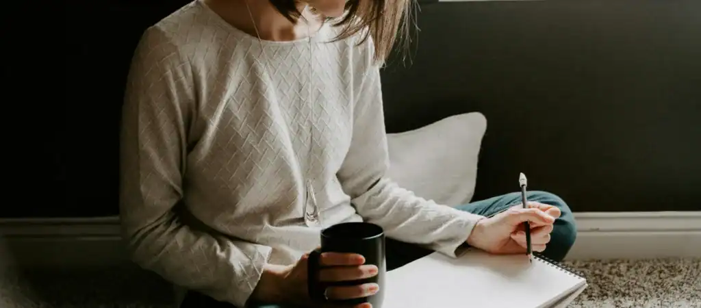 Woman journaling with black coffee on floor