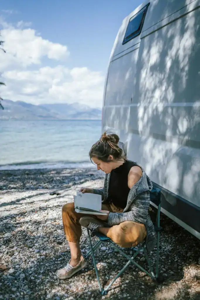 Woman reading by camper at mountain lake
