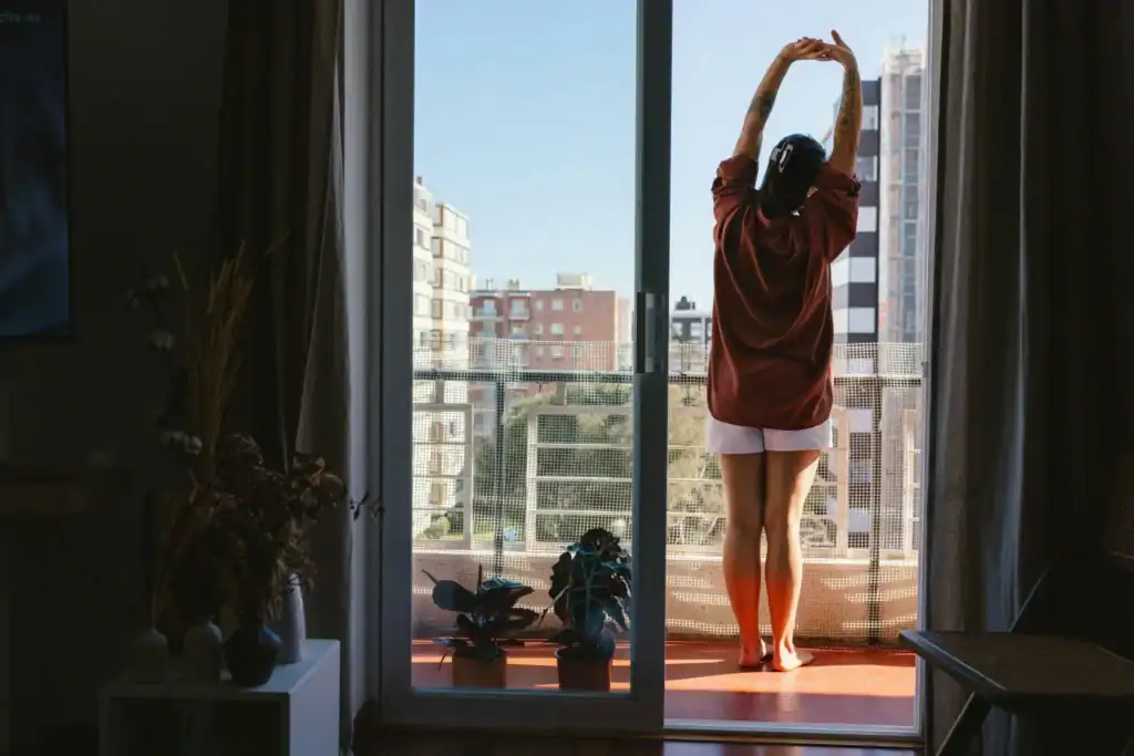 Woman stretching arms up by bright window