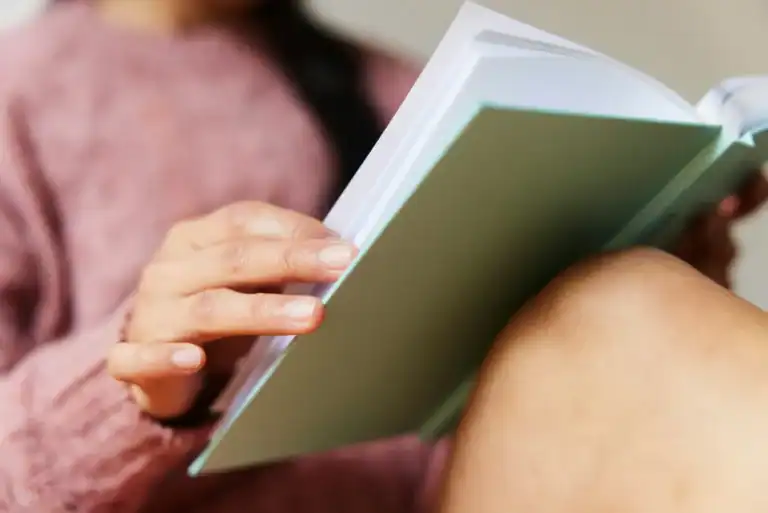 Woman turning page of sage book pink sweater