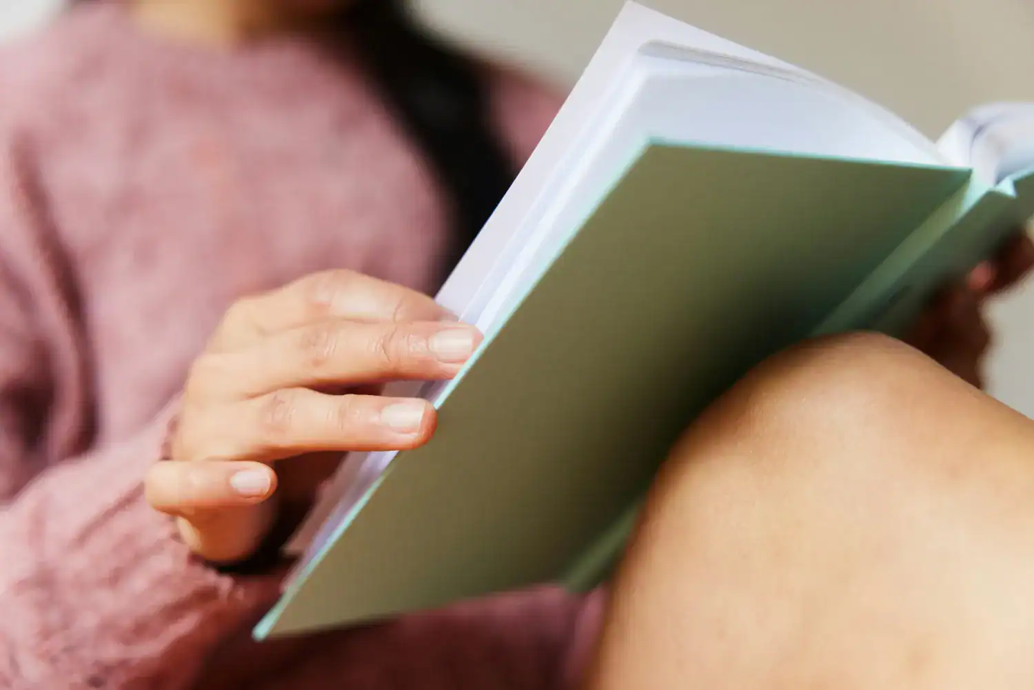 Woman turning page of sage book pink sweater