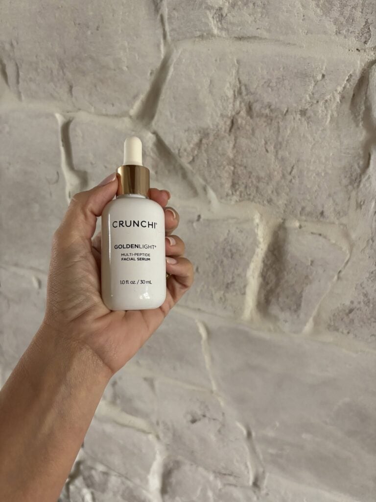 Hand holding a facial serum bottle against a textured wall background.