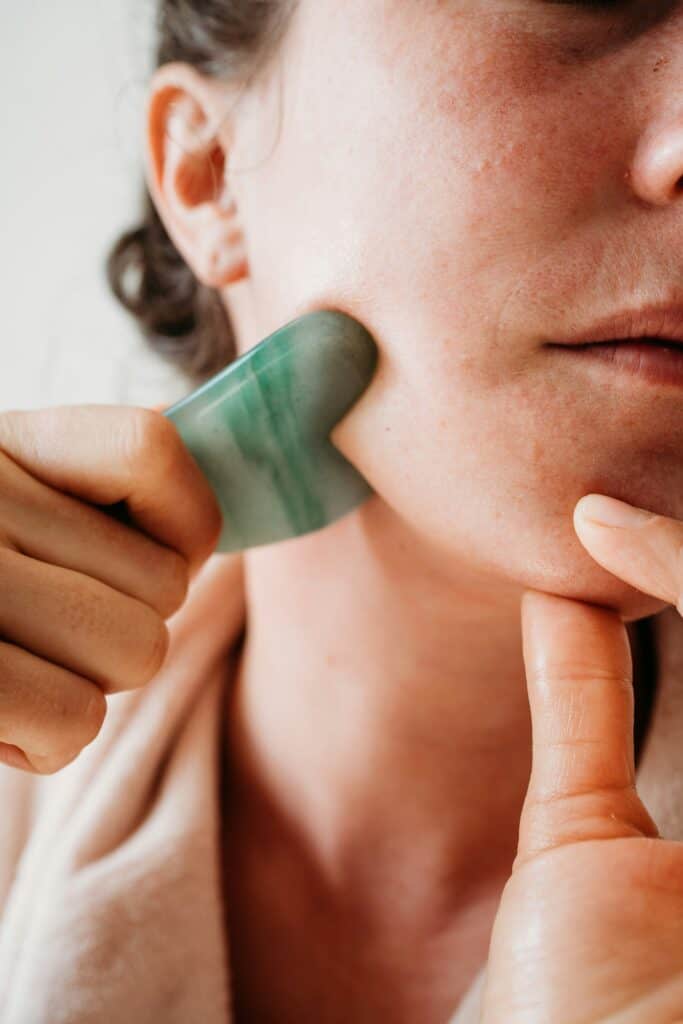 Woman using Gua Sha tool on her face for skin health and relaxation.